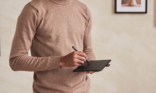Serious young African-American architect in sweater standing in modern office with pictures on wall and drawing maquette in virtual reality goggles